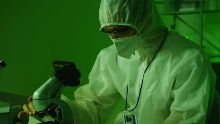 Medical professional in protective gear using a microscope in a laboratory setting.