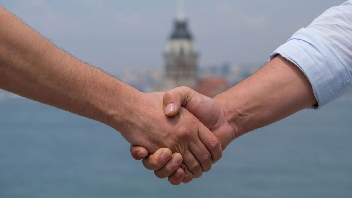 Close-up of handshake at Bosphorus with Maiden's Tower in background, symbolizing cooperation.